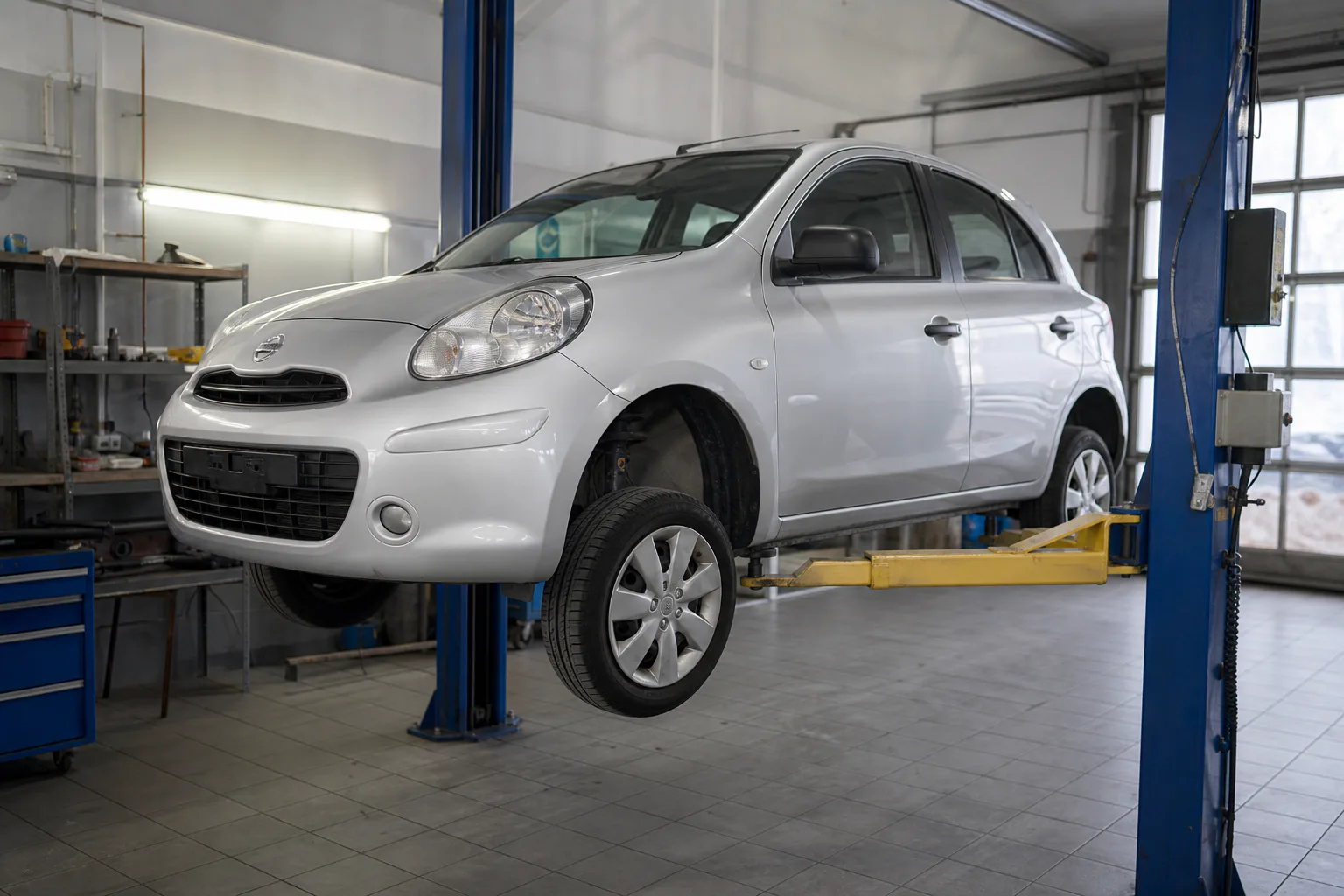 Nissan Micra на подъёмнике при осмотре ходовой и тормозов — иллюстрация